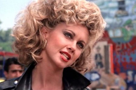 Olivia Newton-John con chaqueta de cuero y cabello rizado junto a John Travolta en una escena de Grease.