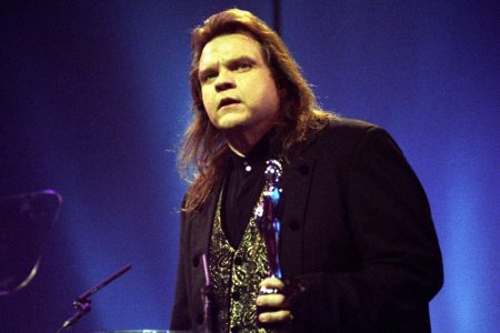 Meat Loaf cantando intensamente al micrófono con camisa de holanes y pañuelo en mano durante un concierto.