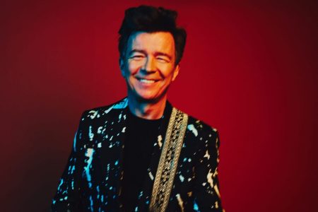 Rick Astley cantando en un escenario con traje durante su época clásica en los años ochenta.