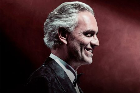 Andrea Bocelli cantando en el escenario con esmoquin negro durante una gala lírica internacional.