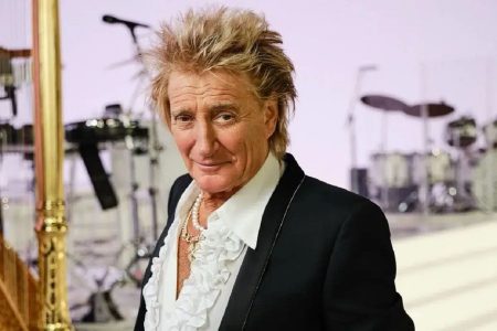 Rod Stewart cantando con traje formal en el escenario durante una presentación en vivo.
