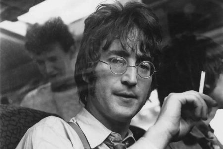 John Lennon cantando al micrófono con gafas redondas en un concierto en Nueva York