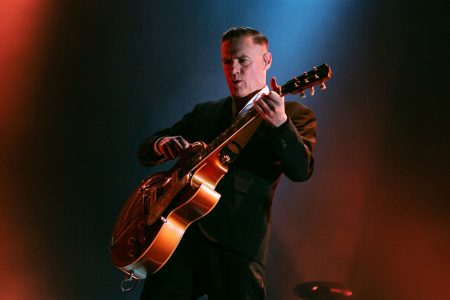 Bryan Adams tocando la guitarra eléctrica con pasión en un concierto en vivo.