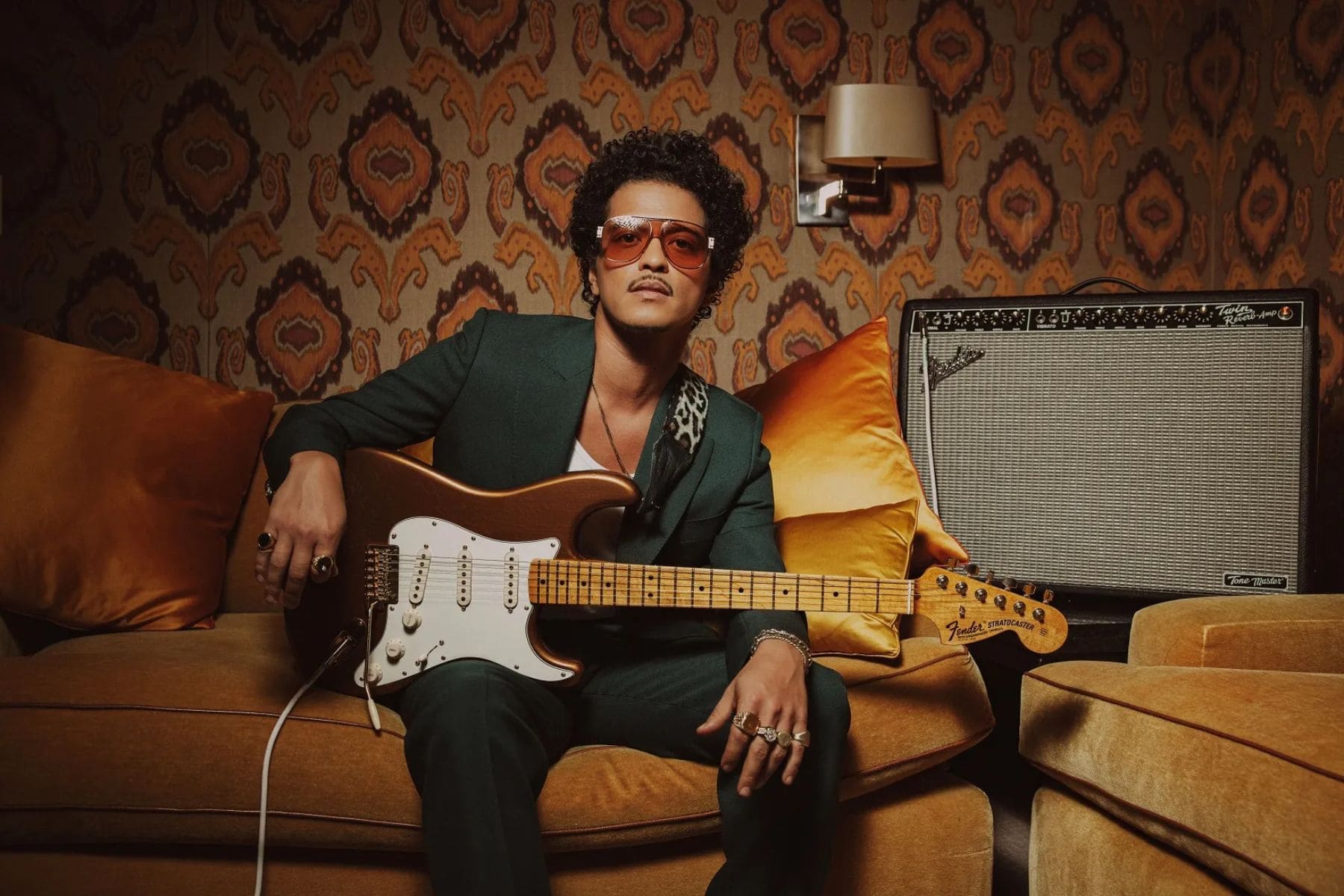 Bruno Mars cantando con sombrero y camisa de seda durante un concierto de funk