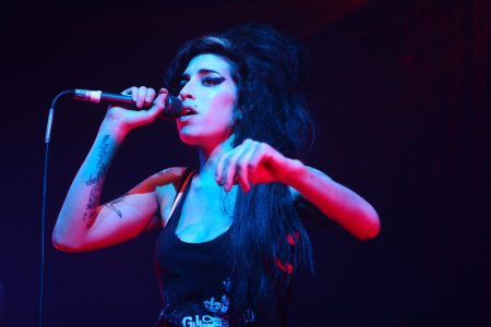 Amy Winehouse cantando con pasión ante el micrófono en un concierto.