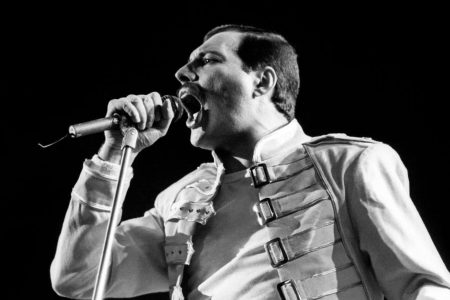 Freddie Mercury sosteniendo el pie de micrófono en el escenario con Queen.